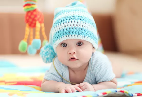 Little Child Lying On A Children's Rug In The White Blue Cap