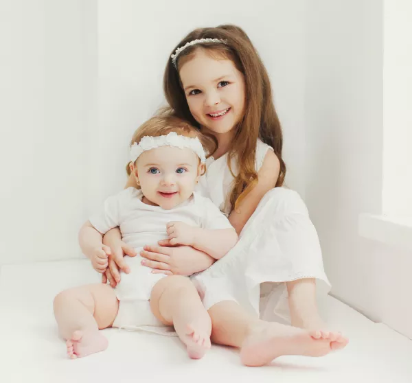 Free Download Portrait Of Cute Little Girl Child With Her Sister Baby Sitting In White Room At Home Near Window - GFXLoad